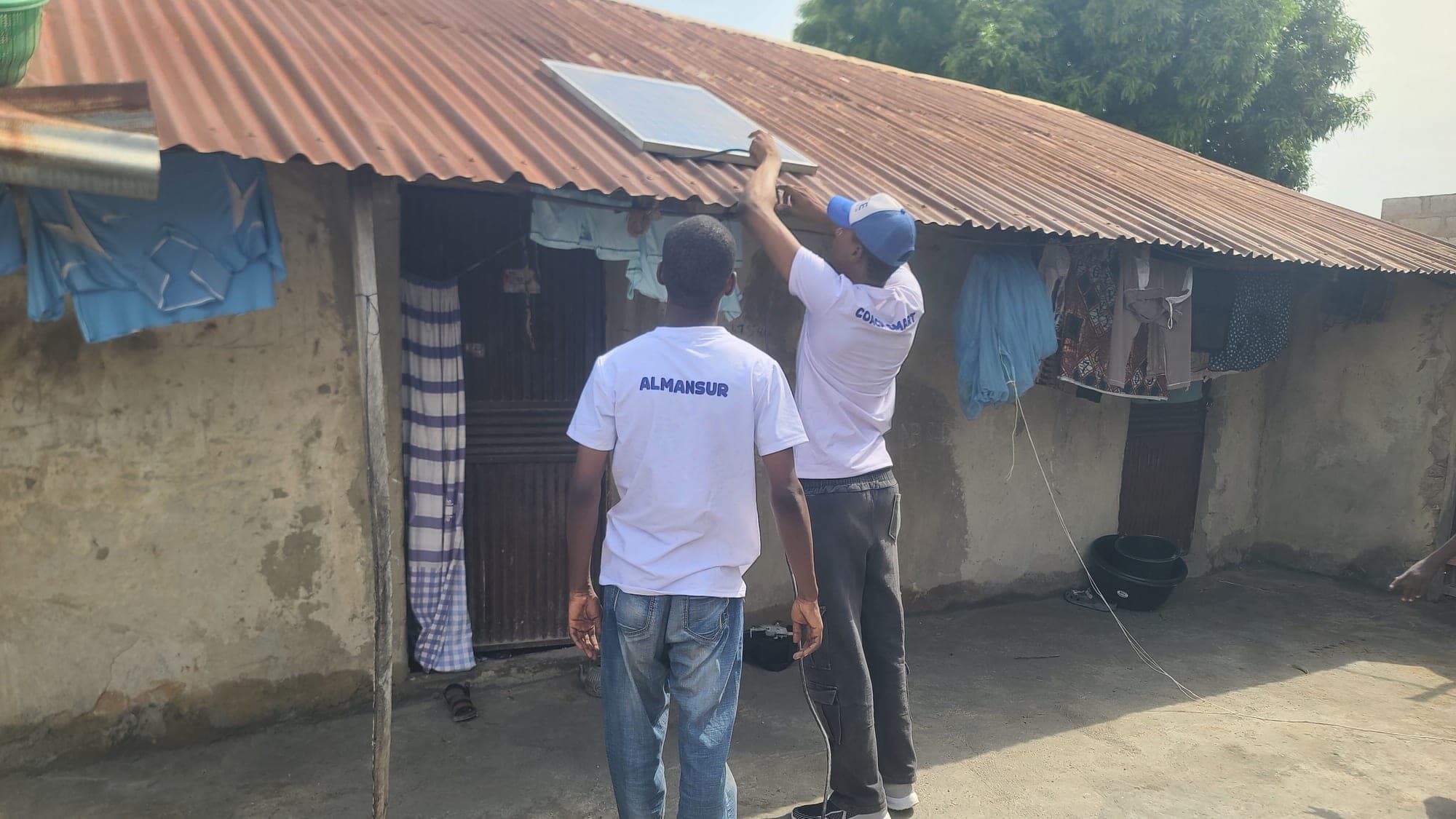 Two SolarPeer team members fit a solar panel to the roof of a house in Minna.